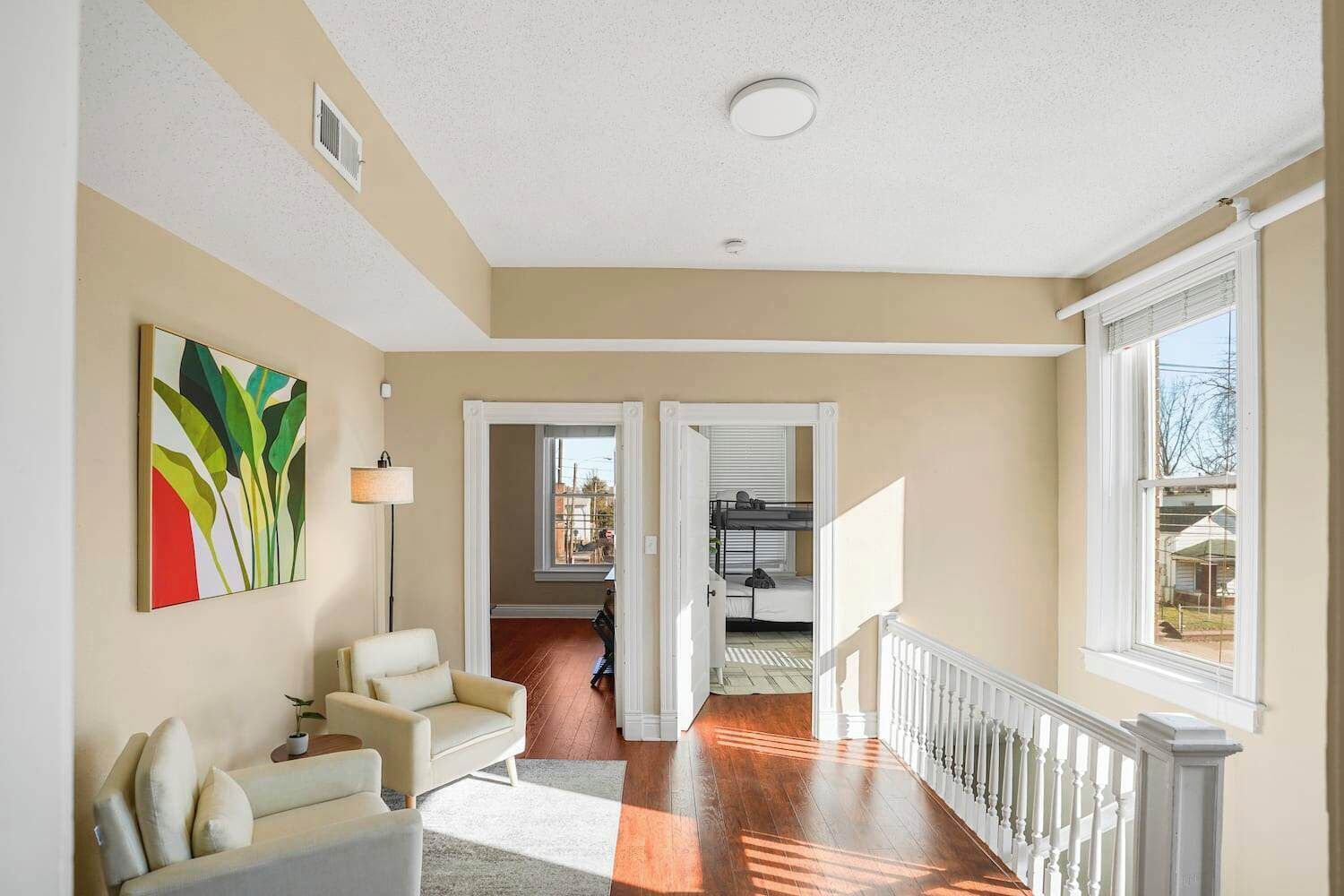 A spacious living room with a beige wall, a colorful abstract painting, a white sofa, and a wooden floor.