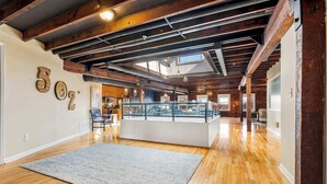 A spacious loft with exposed wooden beams, a central island with glass railings, and a kitchen area in the background. - KING Sleep8 4Bed 3BR 2BA Swepson Loft 301 (Louisville)