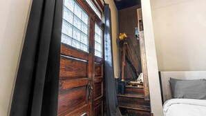 Un dormitorio con puerta de madera, cama con ropa de cama gris y escalera que lleva a un nivel superior.