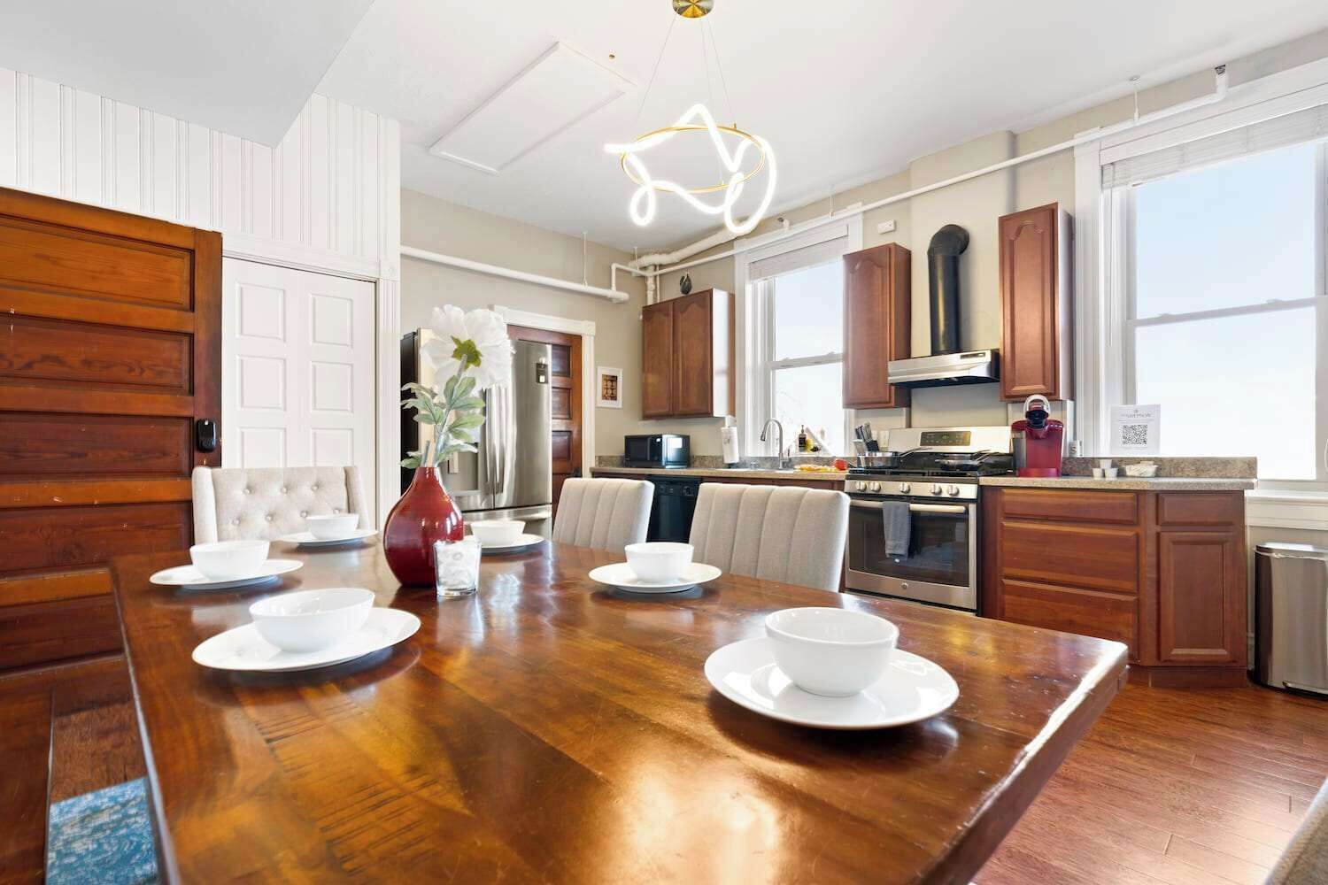 A modern kitchen with wooden cabinets, stainless steel appliances, and a dining area with a wooden table and chairs.