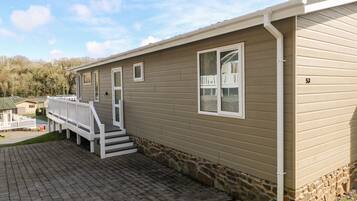 A single-story mobile home with a stone foundation, a front porch with white railings, and a number '53' on the side.