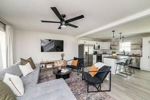 A modern living room with a grey sofa, black chairs, a coffee table, and a ceiling fan.