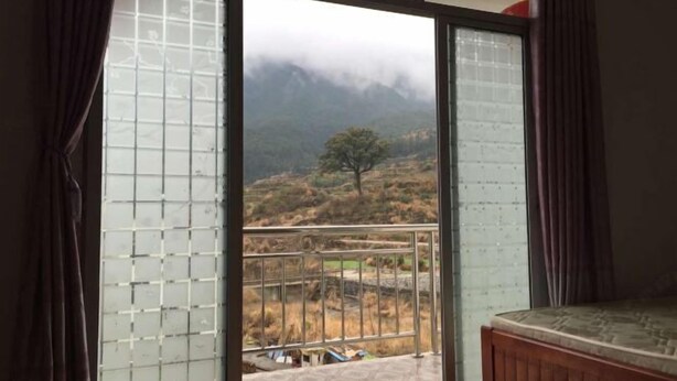 Una habitación con cama, ventana con vistas a un paisaje montañoso y balcón con barandilla.
