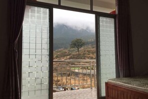 Una habitación con cama, ventana con vistas a un paisaje montañoso y balcón con barandilla.