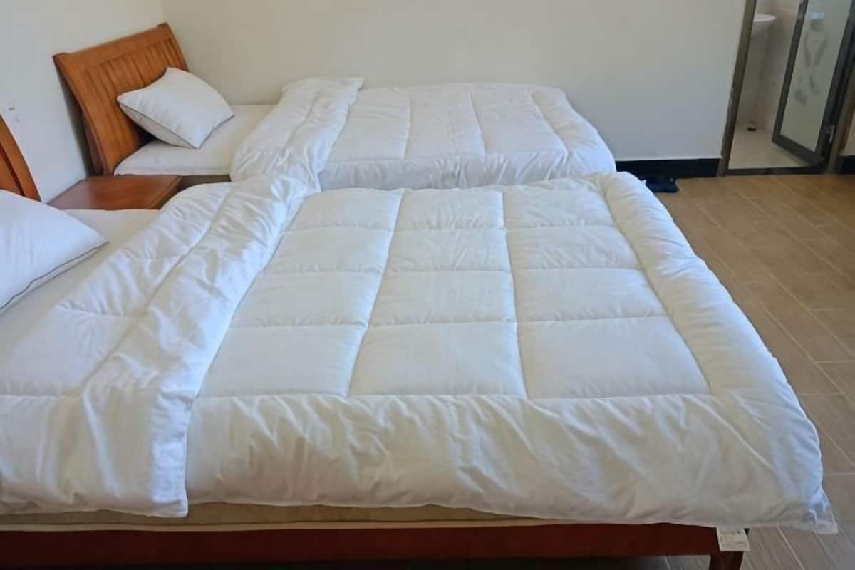 A bed with a white quilt, a wooden headboard, and a wooden nightstand with a lamp.