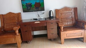 Un escritorio de madera con cajones, una silla, un televisor montado en la pared y un hervidor.