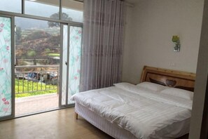 Un dormitorio con una cama, vistas a través de un ventanal corredera y un pequeño florero verde en la pared.