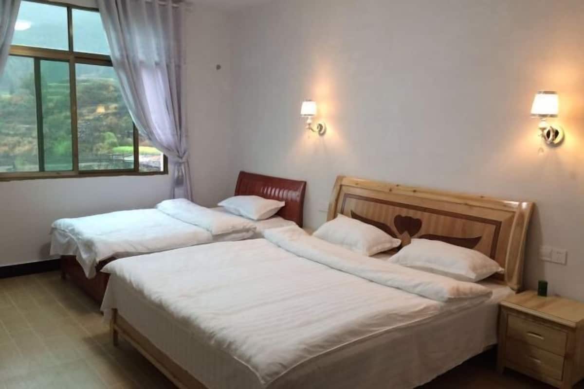 A hotel room with two single beds, a wooden headboard, bedside lamps, a nightstand, and a window with curtains.