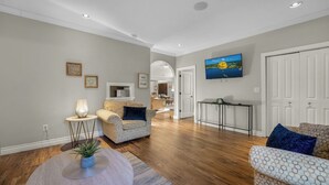 Ein geräumiges Wohnzimmer mit Holzdielen, einer Couch, einem Couchtisch und einem an der Wand montierten Fernseher.