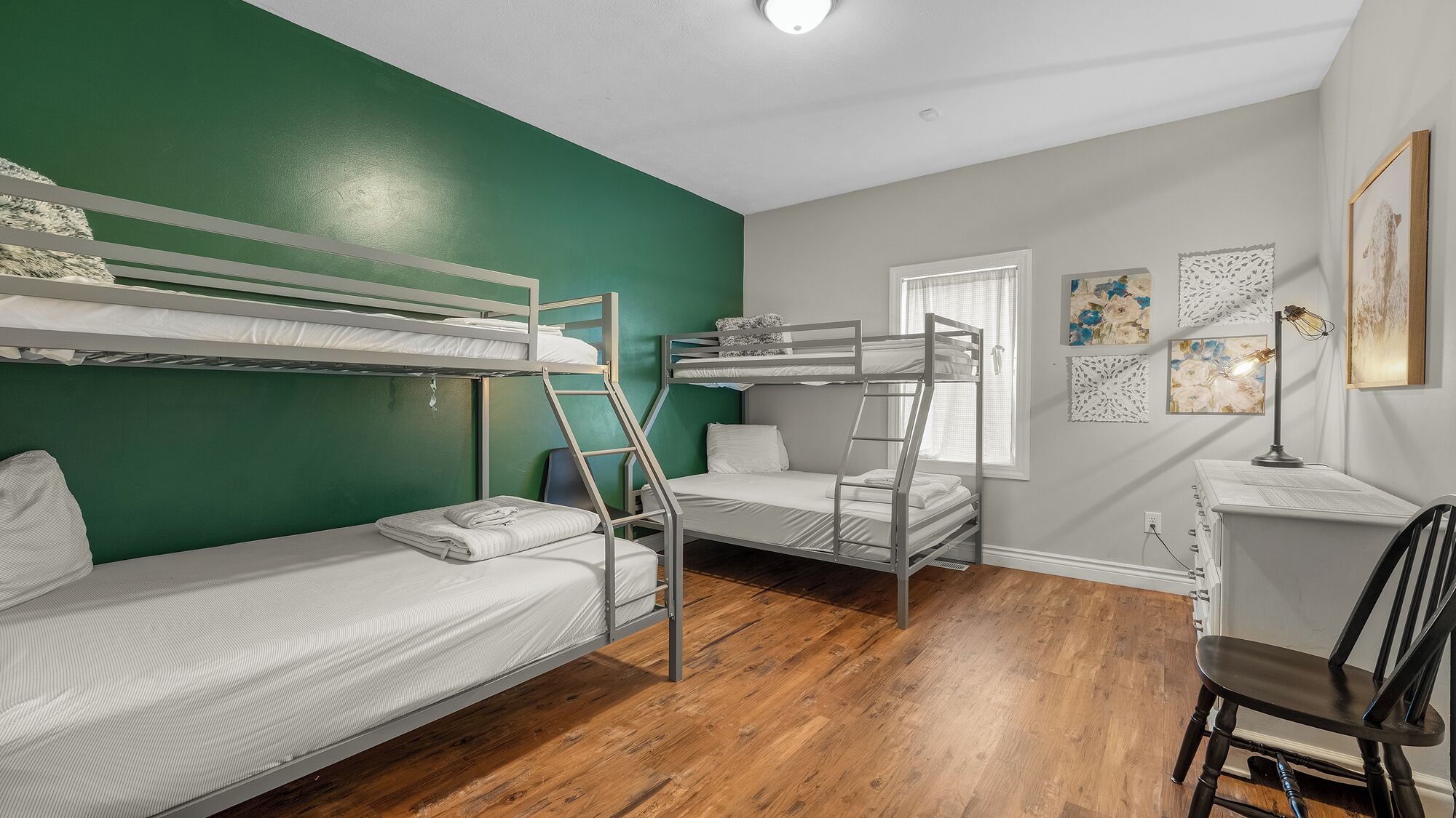 A dormitory room with bunk beds, a desk, a chair, and artwork on the walls.