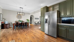 Eine moderne Küche mit Holzboden, grünen Schränken, Edelstahlgeräten und einem Essbereich mit Holztisch und Stühlen.