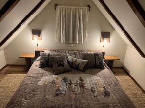 A cozy attic bedroom with a large bed, two bedside tables, and a window with curtains.