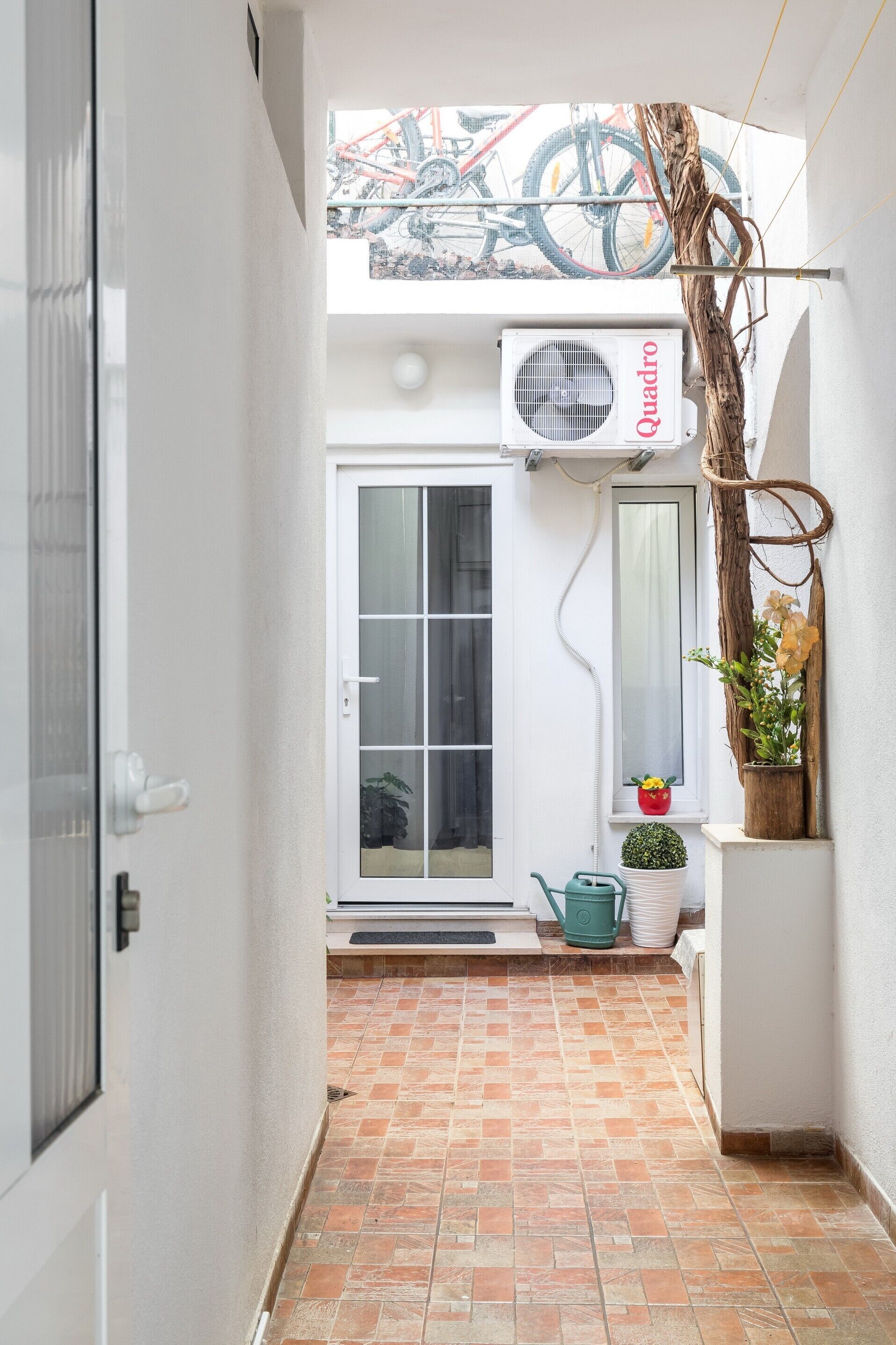 A narrow hallway with a tiled floor, a white door, and a window with a view of bicycles and a building.