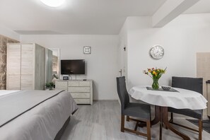 A bedroom with a bed, a dresser, a TV, a dining table with chairs, and a clock on the wall.
