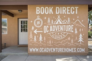 A brown sign with white text for OC Adventure Homes, featuring a compass, trees, and a tent.