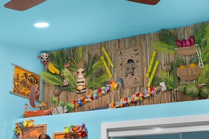 A room with a blue wall, decorative masks, a woven bamboo backdrop, and a lei garland.