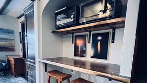 Une cuisine compacte dotée d’un four à micro-ondes encastré, d’un petit plan de travail et de deux tabourets en bois.