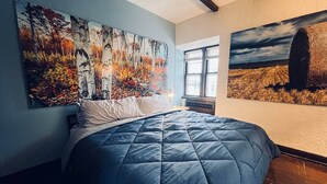 Une chambre avec un grand lit, deux tableaux accrochés aux murs et une fenêtre laissant entrer la lumière naturelle.