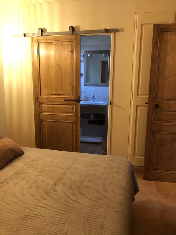Un dormitorio con cama, un armario de madera y un baño visible a través de una puerta abierta.