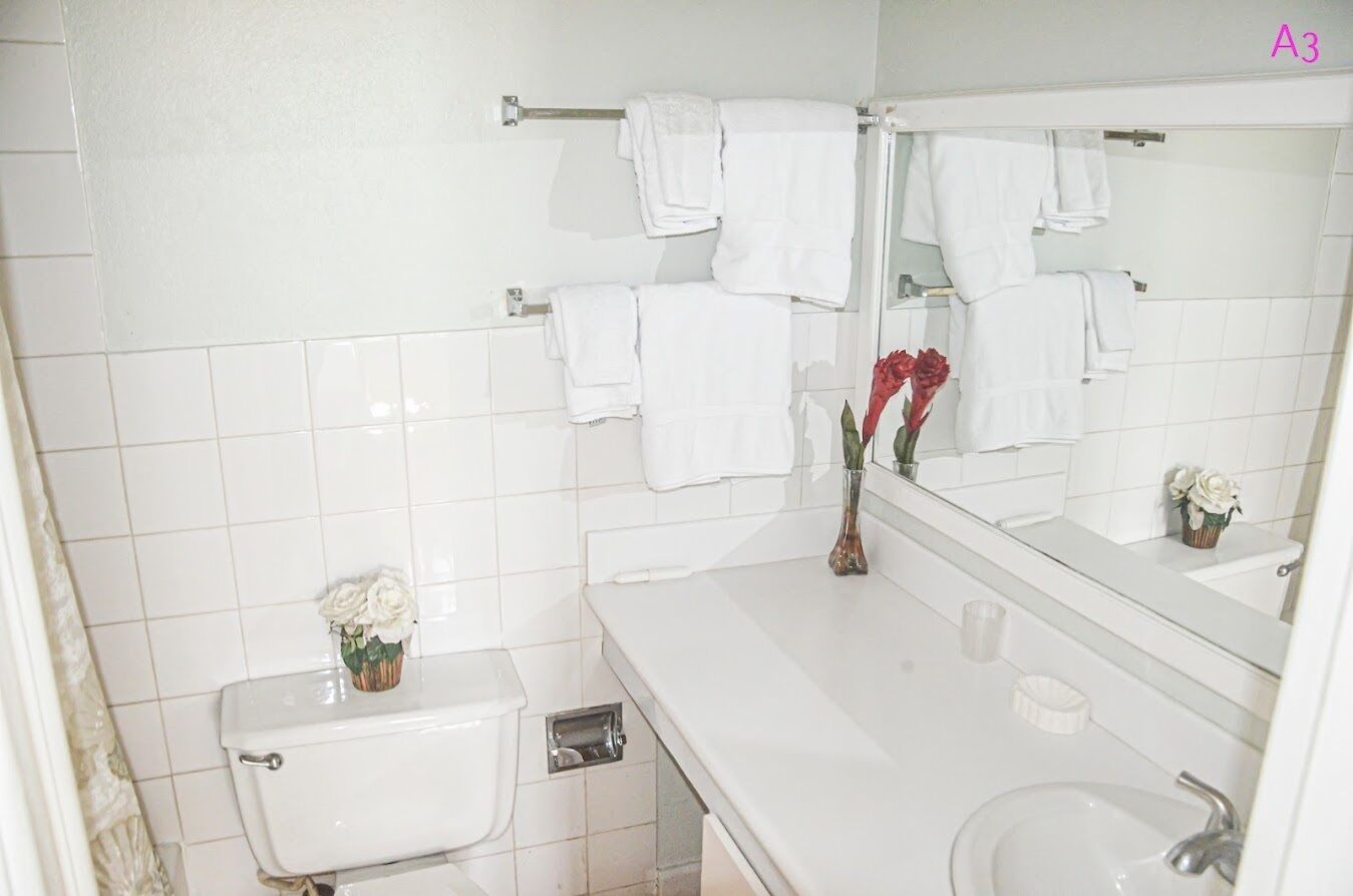 Un baño con azulejos blancos, un inodoro, un lavabo, un espejo y toallas colgadas en un perchero.