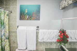 A bathroom with a seahorse painting, white towels, and a vase of red roses.