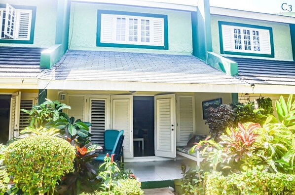 A two-story house with a covered porch, white doors, and a green roof.