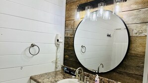 Ein Badezimmer mit einem weißen Waschbecken, einem runden Spiegel und einem Föhn an der Wand.