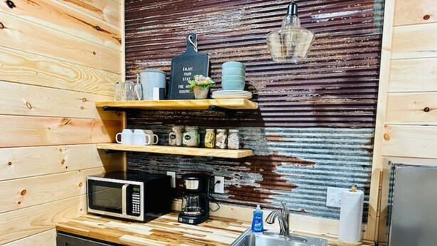 Eine kleine Küche mit Holzschränken, einer Mikrowelle, einer Kaffeemaschine und einem Spülbecken.