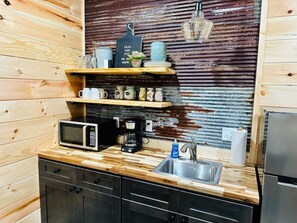 A compact kitchen with wooden cabinetry, a microwave, a coffee maker, and a sink. - Knotty Squirrel Unit 8 Standard King Suite (Mountain View)