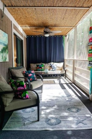 A sunroom with a ceiling fan, a sofa with cushions, a coffee table, and a patterned rug.