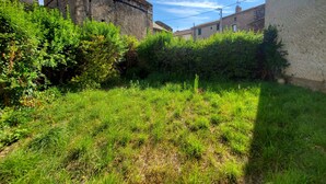 Ein Steinhaus mit Glockenturm, umgeben von üppiger Vegetation und angrenzenden Wohngebäuden.