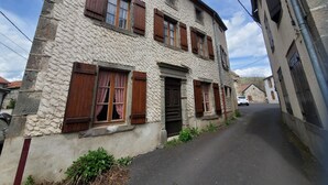 Ein zweistöckiges Steinhaus mit Holzläden, eine schmale Gasse und ein geparktes Auto.