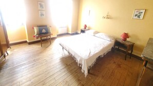 Ein Zimmer mit Holzboden, einem Bett mit weißer Bettdecke, einer Bank mit Kissen und einer Wandleuchte.