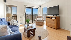 A living room with a sofa, a coffee table, a chair, a television, and a wooden cabinet. - Duckburgh - Ocean view, Updated, 2 min. walk to the beach (Kitty Hawk)