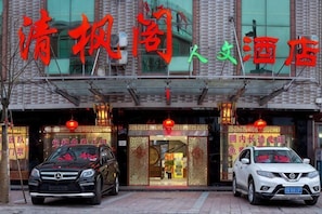 A hotel entrance with a signboard, two cars parked in front, and traditional Chinese decorations.