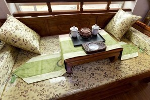 A wooden bench with patterned cushions, a tray with teapots and a teapot, and a window with a view.