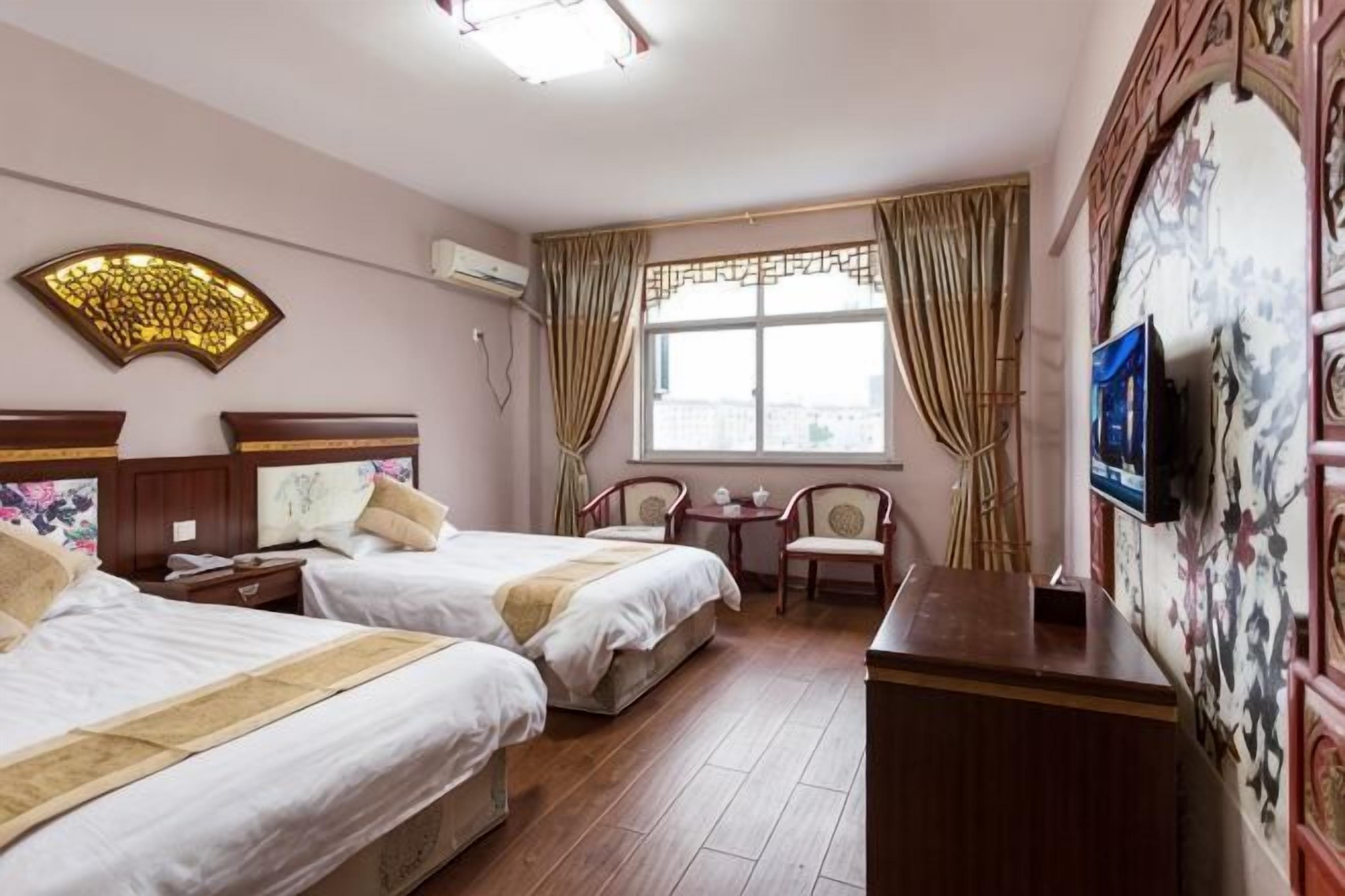 Une chambre d’hôtel avec deux lits, une petite table, une chaise et un téléviseur fixé au mur.