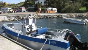 A small motorboat docked at a wooden pier with a rocky shoreline and houses in the background. - Remarkable 2-bed Apartment in Steinsland (Oygarden)