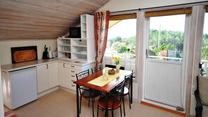 A compact kitchen with white cabinets, a wooden dining table, and a view of greenery through the window. - Remarkable 2-bed Apartment in Steinsland (Oygarden)