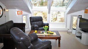 A cozy living room with a high ceiling, a large window, a black leather sofa, a leather armchair, a wooden coffee table with fruit, and a television on a stand. - Remarkable 2-bed Apartment in Steinsland (Oygarden)