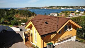 A yellow house with a brown roof, a covered patio, and a view of the sea and hills in the background. - Remarkable 2-bed Apartment in Steinsland (Oygarden)