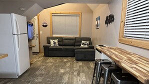 Une cuisine compacte équipée d’un réfrigérateur, d’un plan de travail en bois et d’un canapé agrémenté de coussins décoratifs.