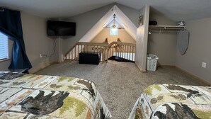 Une chambre avec deux lits, un téléviseur, un ventilateur de plafond et un escalier menant à un étage supérieur.