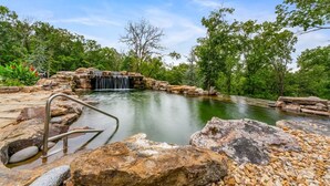 A natural pool with a waterfall, surrounded by rocks and trees.