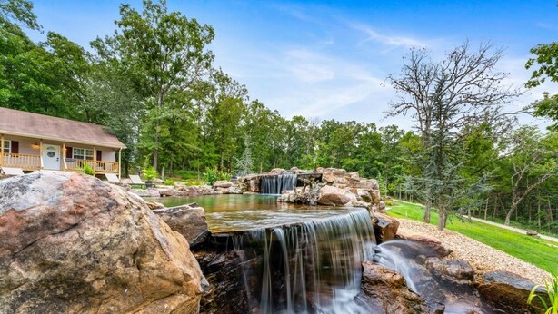 A lodge with a waterfall, surrounded by trees and a well-maintained lawn.