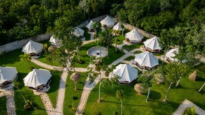 Une vue aérienne d’un complexe touristique composé de plusieurs tentes en forme de dôme, disposées autour d’un espace circulaire central, le tout entouré d’une végétation luxuriante et d’un mur de pierre.