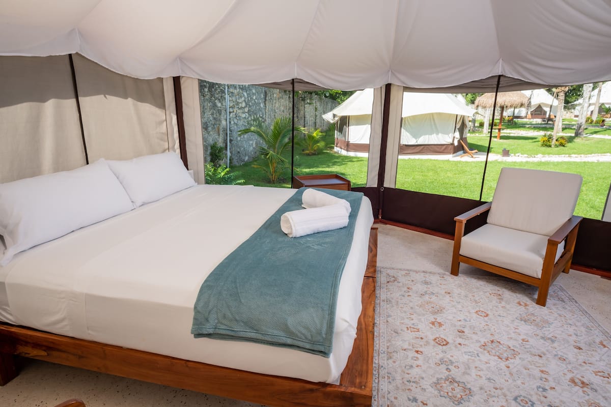 A bedroom with a bed, a chair, and a view of a garden.