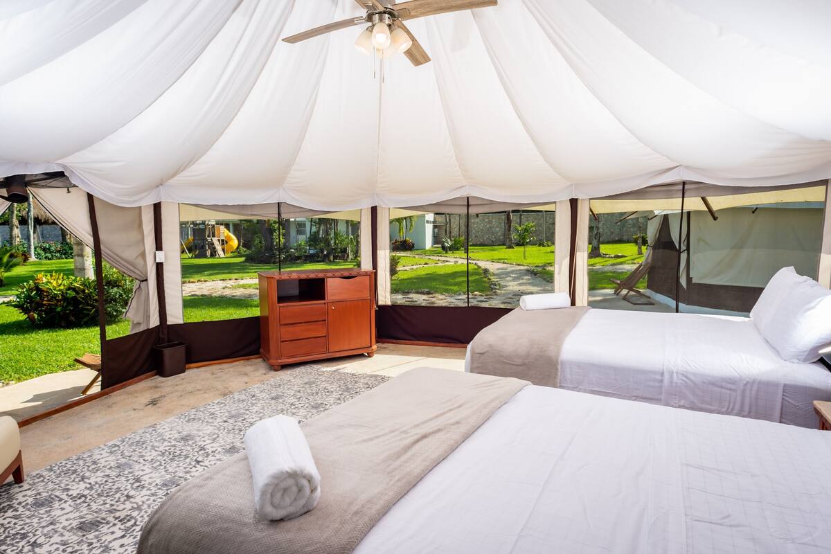 A tented room with two beds, a wooden dresser, and a view of a garden.