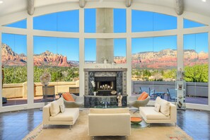Amplia sala de estar con chimenea, dos sofás y un ventanal con vistas a formaciones rocosas rojas.