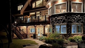 A multi-story house with a stone facade, a wooden deck, and a stone pathway leading to the entrance. - 6 bed 4 bath cottage on Lake Muskoka, Private, Boathouse, Hot tub! (Gravenhurst)